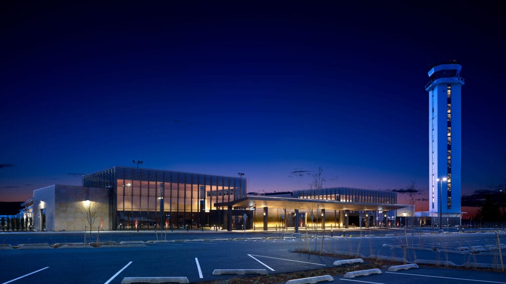Exterior of Paine Field passenger terminal at night with interior lights on and next to air traffic control tower