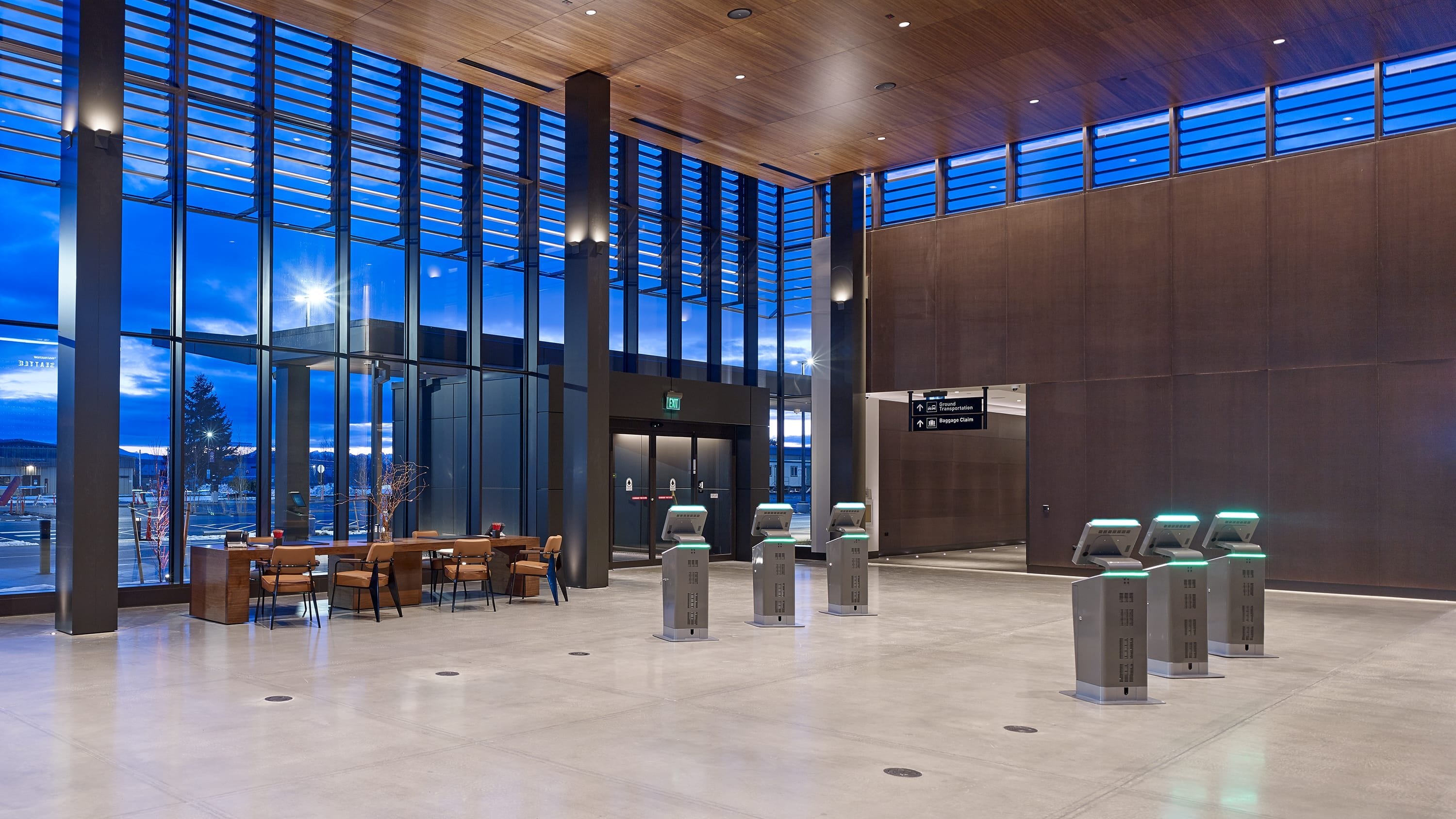 Interior of Paine Field passenger terminal ticketing hall with modern wood-paneled ceilings, floor-to-ceiling windows, seating, and automated passenger screening gates